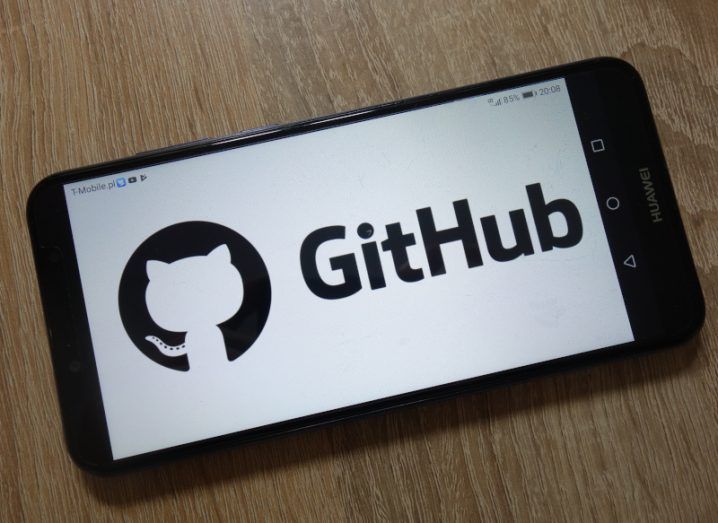 The GitHub logo on a smartphone screen, which is laying on a brown wooden background.