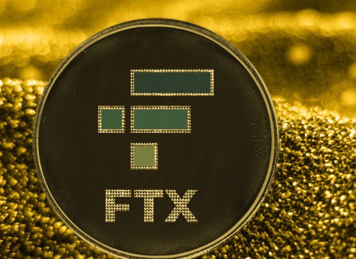 A black coin with the FTX logo on its front, with a gold grain background.