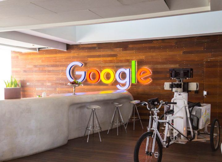 A Google logo on an office wall, behind a table counter and a bike. Google is owned by Alphabet.