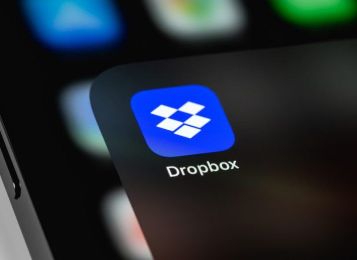 Dropbox logo on a mobile phone screen, with other app icons blurred in the background.