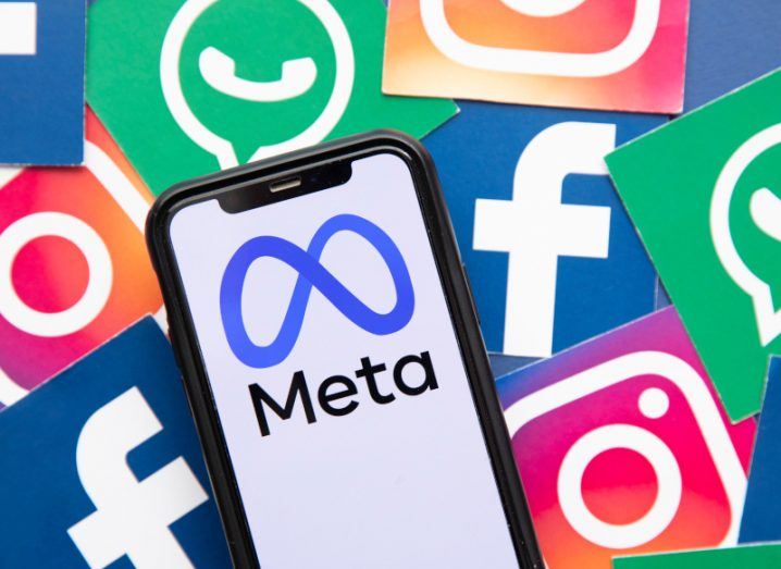 A phone displaying the Meta logo on its screen lays on top of a pile of paper cut-outs of the Instagram, WhatsApp and Facebook app icons.