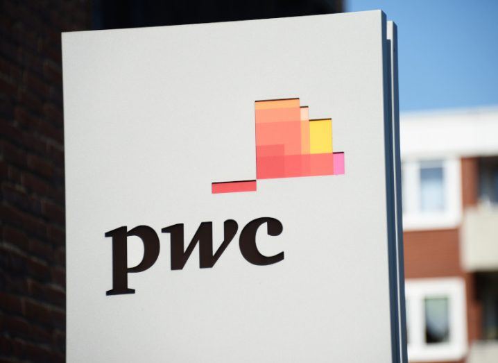 The PwC logo on a white sign with buildings in the background.