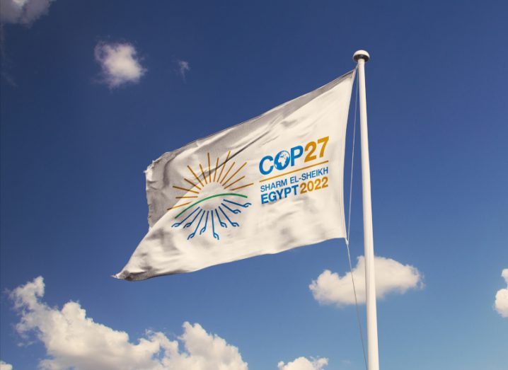A flag for COP27 flies against a blue sky.