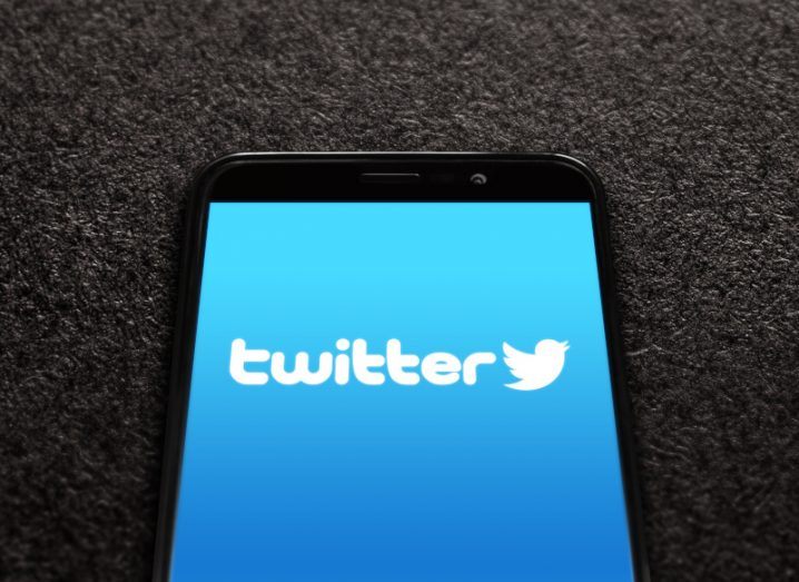 Twitter logo on a mobile phone screen laying on a brown carpet background.