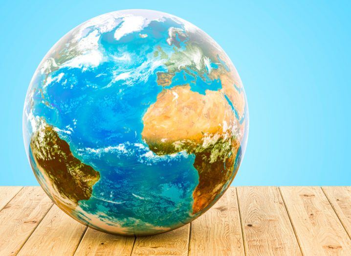 A globe of the Earth with continents such as Europe and Africa visible. The globe is resting on a wooden table with a blue wall background.