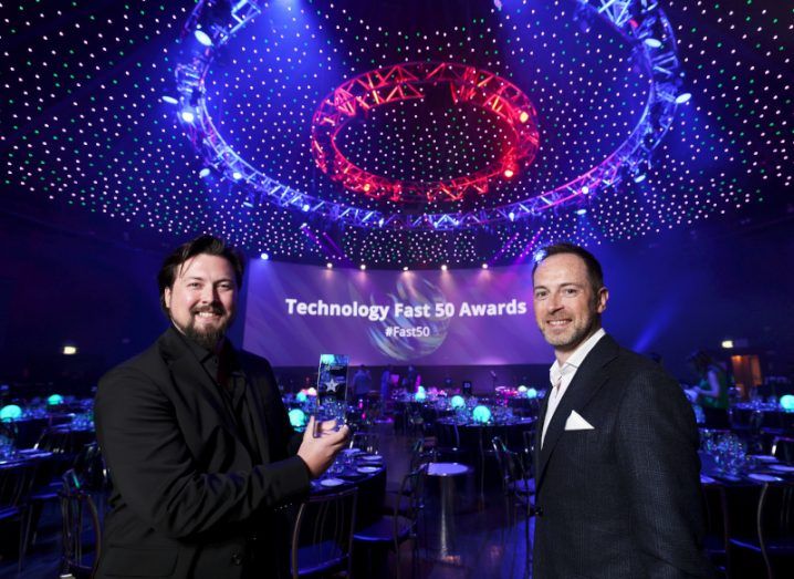 Buymie's Devan Hughes stands holding an award at an event, with Deloitte's David Shanahan standing beside him.