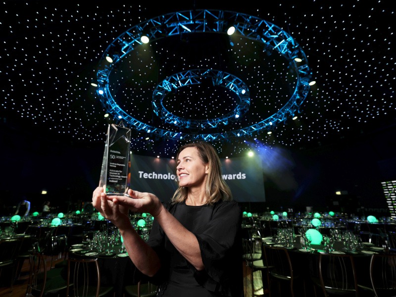 Swoop's Andrea Reynolds stands holding an award at the Deloitte event.