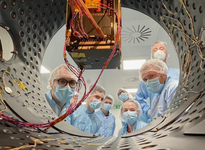 A team wearing protective gear with the European Space Agency logo examines the Eirsat-1 satellite.