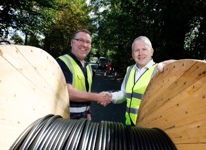 Two men standing in front of a wooden spool that has a roll of black cables. They are executives of Total Splicing Solutions and Speed Fibre Group, which Enet is a part of.