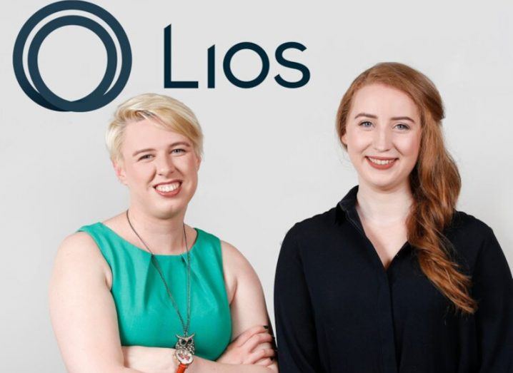 Two women standing in front of a grey wall with the Lios logo on it. They are the co-founders of Lios.