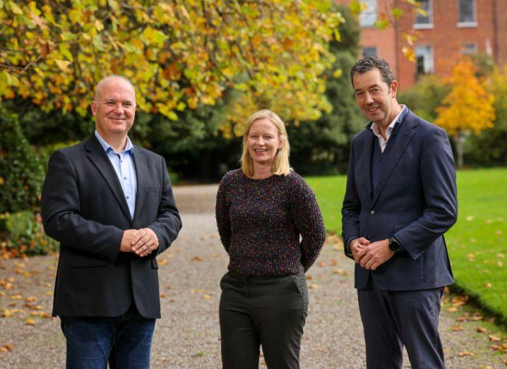Dr Tony Holohan, Dr Aine Adams and Gary McAuslan stand in a line outdoors with trees behind them.