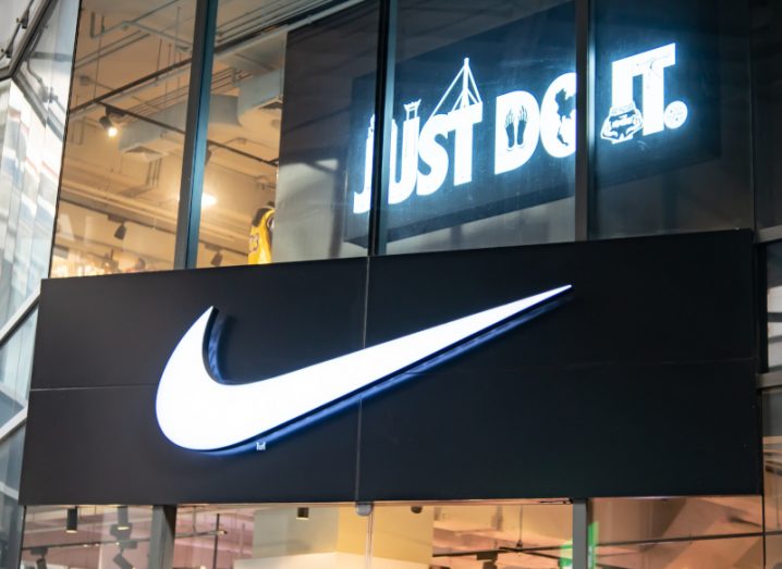 Nike logo in front of a shop with a sign inside that reads "Just do it".