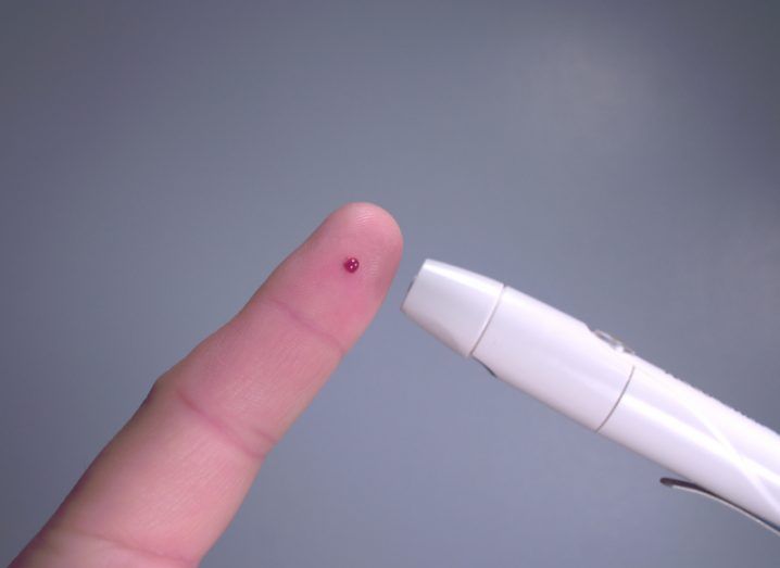 Photo of a fingertip pierced by glucose meter with a tiny drop of blood showing.