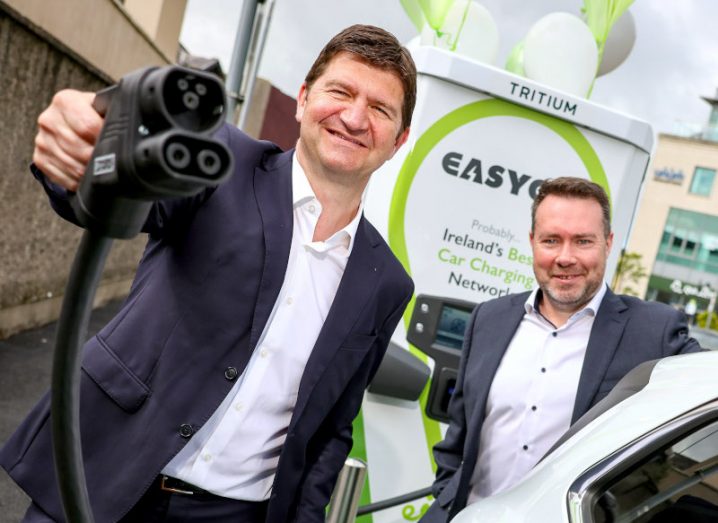 Two men wearing suits in front of an EasyGo charger.