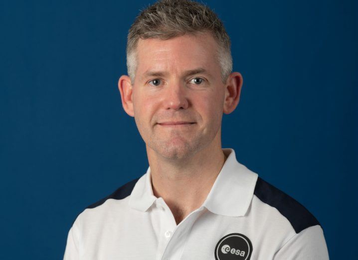 Headshot of John McFall wearing an ESA shirt in front of a blue background.