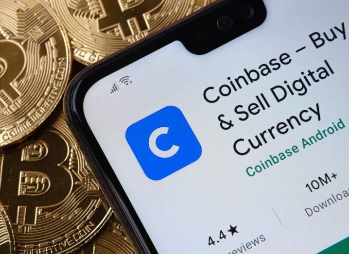 A phone showing the Coinbase app. The phone lies on top of several gold bitcoins.