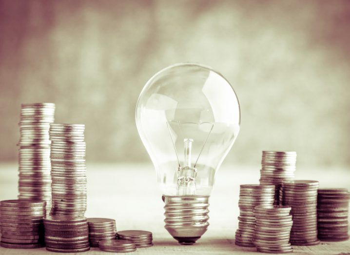 A light bulb resting on a table with piles of coins next to it.