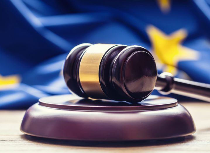 Wooden gavel resting on a table with an EU flag in the background.