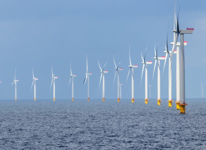 Offshore wind farm with wind turbines in a row and the sea and sky visible.
