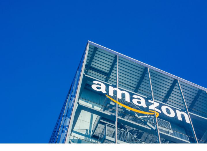 Amazon logo on a grey building pictured against a blue sky.
