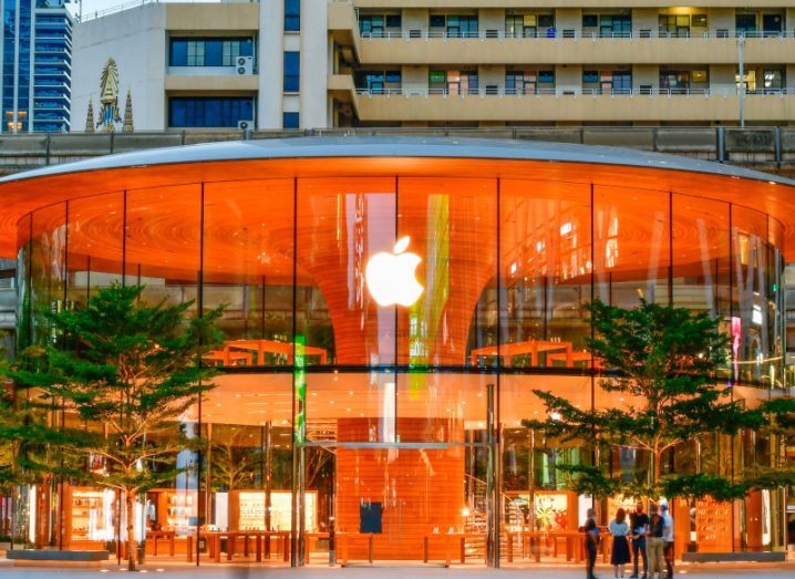 A store with the Apple logo on the window. The store is surrounded by windows, with a large column at the center and a wide dome roof. There are two trees in front of the building.