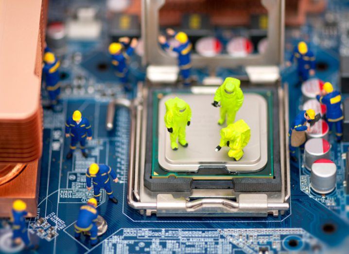 Miniature figures wearing fluorescent hazmat suits inspect a computer motherboard.