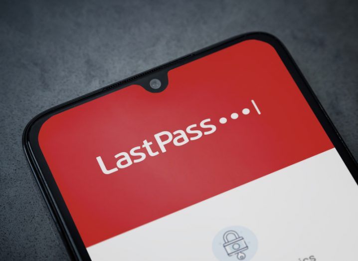 LastPass company logo on the smartphone screen, with a small lock sign on the lower end of the phone screen. The phone is laying on a grey surface.