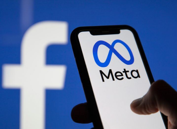 Meta logo on a smartphone in a person's hand, with the Facebook logo in the background.