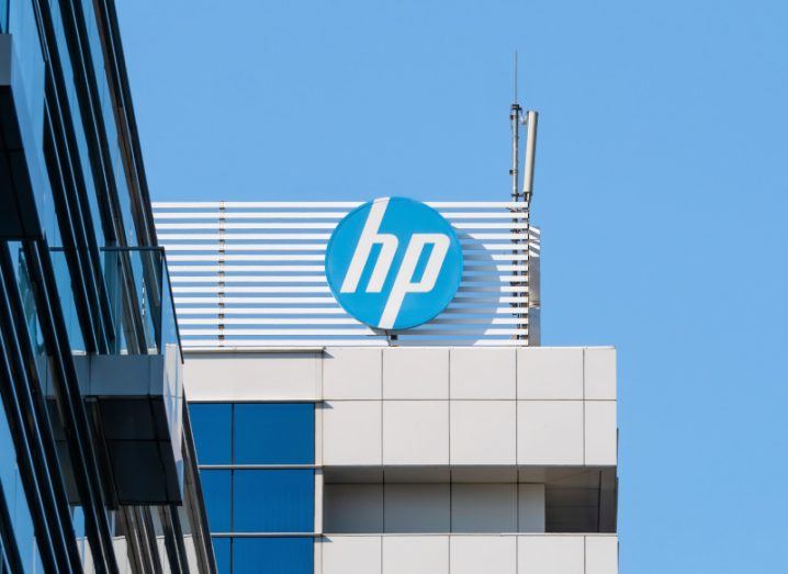 The HP logo on the side of a grey building, with a clear blue sky behind it.