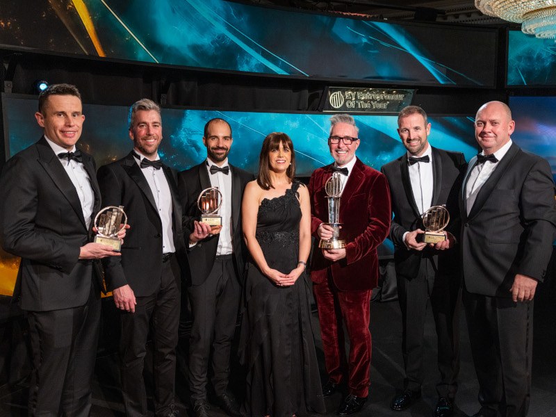 The winners of the EY Entrepreneur of the Year awards stand in a line with their trophies.