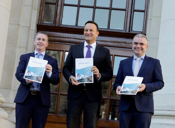 The three ministers stand outside Government buildings holding up the white paper on enterprise.
