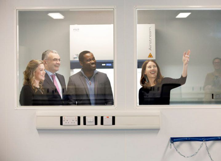 Two men and two women are visible through the window of a wet lab. They are getting a tour of The Campus life sciences facility in south Dublin.