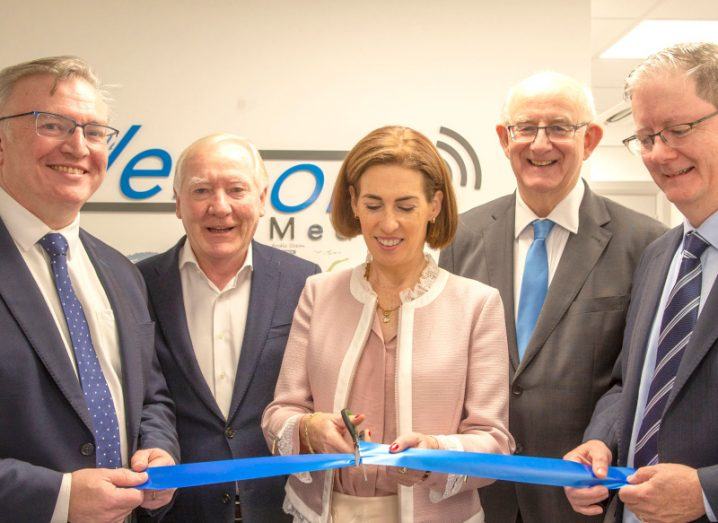 Four men holding a blue ribbon as a woman in the centre cuts it with a scissors. The Versono Medical logo is visible on a wall in the background.