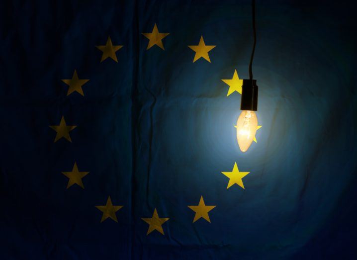 A glowing lightbulb with the EU flag partially visible behind it.