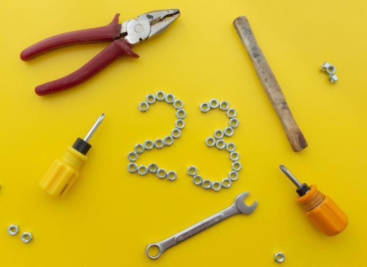 The number 23 on a yellow background with tools such as wrenches and screwdrivers all around it.