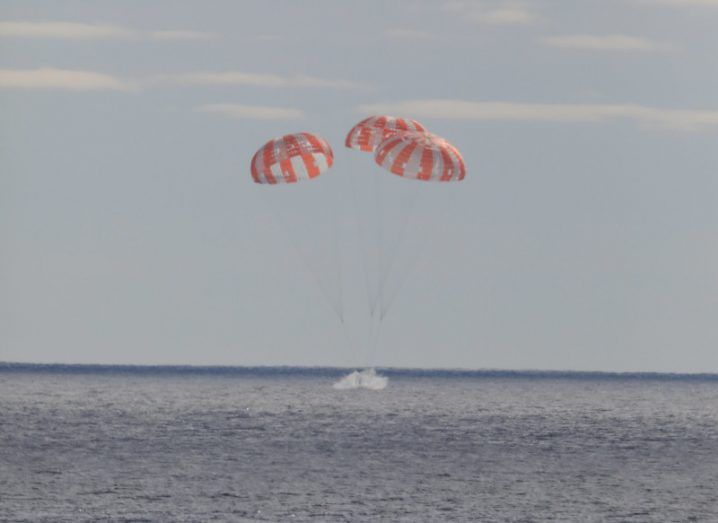 A spacecraft landing in the ocean with three red and white parachutes connected to it. It is NASA's Orion capsule.