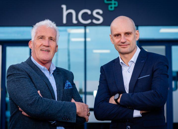 Mick Foley of Fixaphone and Sean Hegarty of HCS standing next to each other wearing suits. There is a building in the background with the HCS logo visible above some windows.
