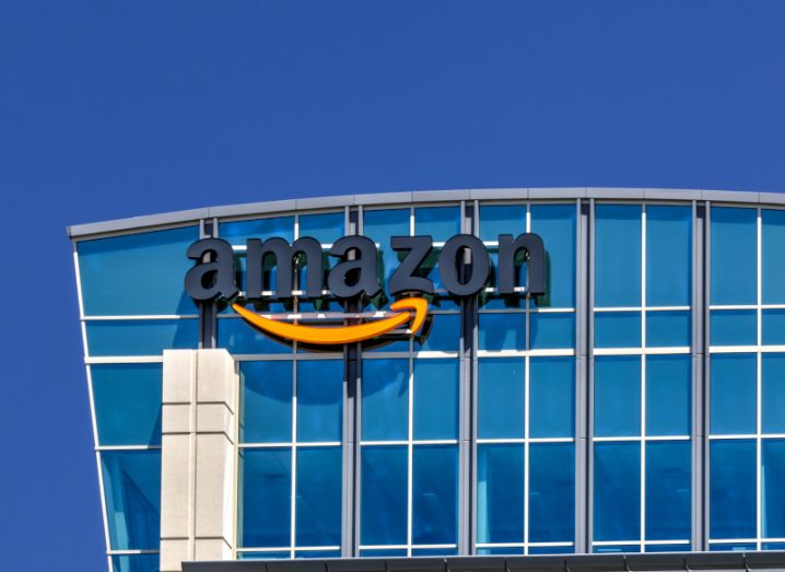 Amazon logo on the side of a blue windowed building, with a blue sky in the background.