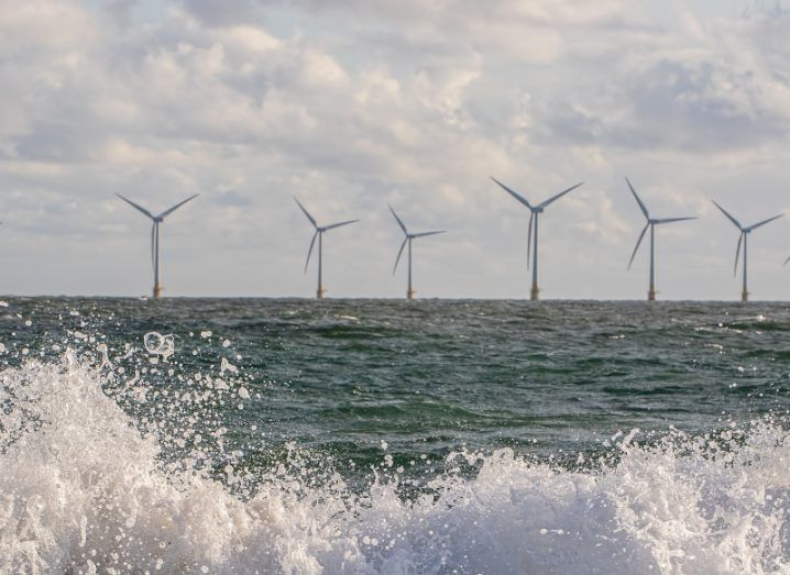 An offshore wind farm with wind turbines visible on a coastline and waves crashing towards the shore.