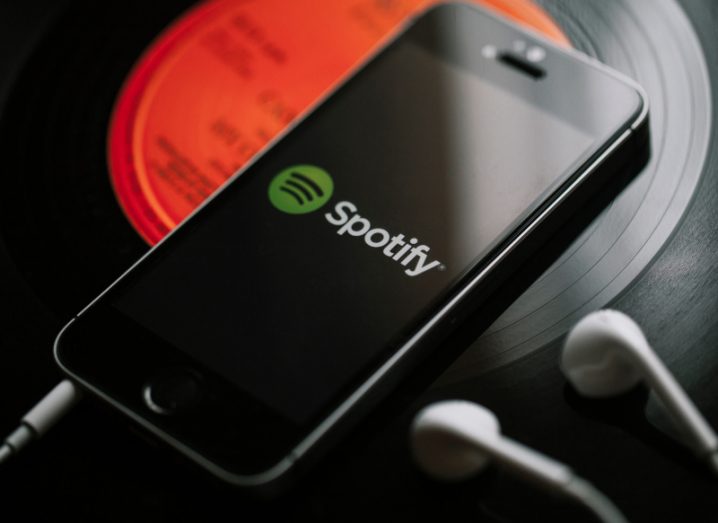 Spotify logo on a smartphone screen. The phone is laying on a vinyl record and is next to a pair of earphones.
