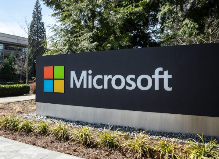 Microsoft logo on a black sign, with trees behind it and a building in the left background.