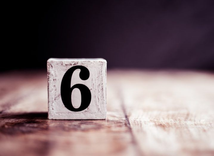 A white block bearing the number 6 placed on a wooden table.