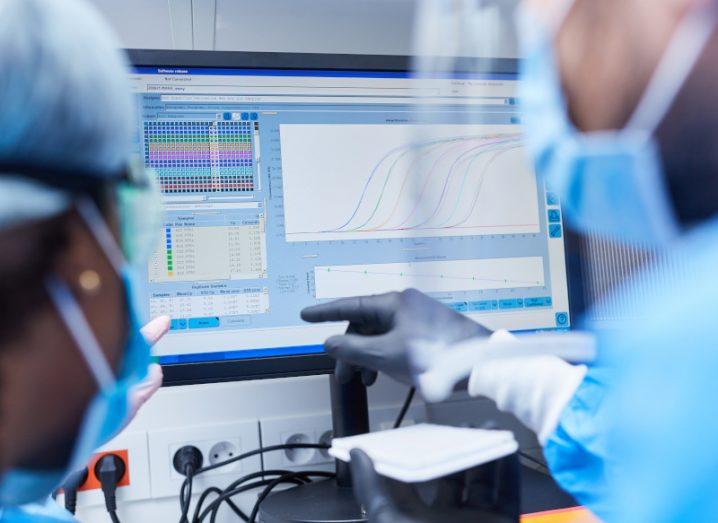 Two researchers wearing face masks looking at data on a computer screen, with one of the researchers pointing at the screen.