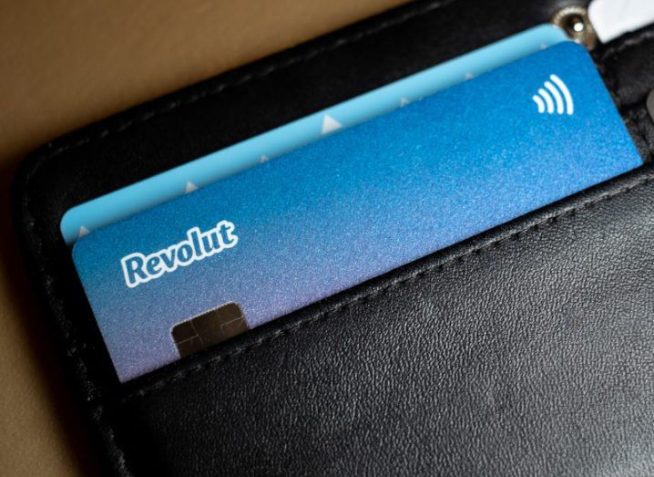A Revolut card inside a black wallet, which is laying on a brown wooden surface.