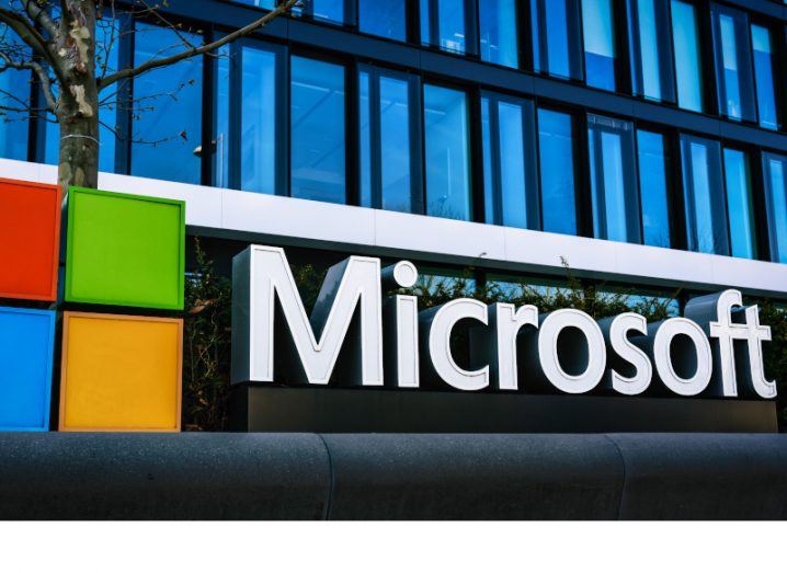 The Microsoft logo on the front of a building with the windows visible in the background.