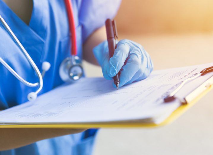 A doctor writing on a piece of paper attached to a clipboard, wearing blue surgical gloves.