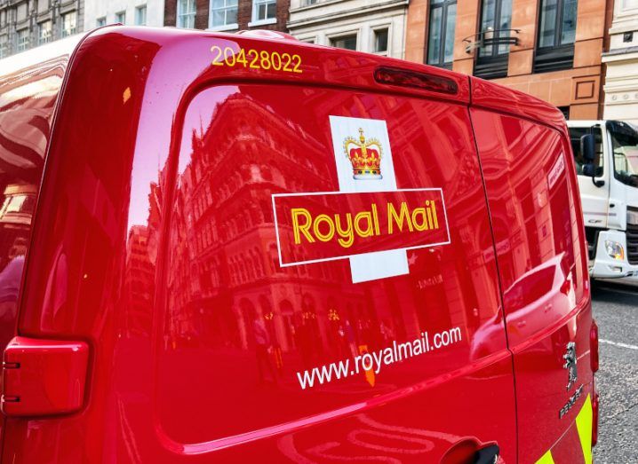 Royal Mail logo on the back of a red van, with buildings in the background.