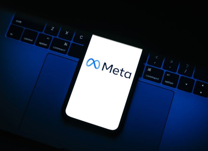 Meta logo on a smartphone screen, which is laying on a laptop keyboard.