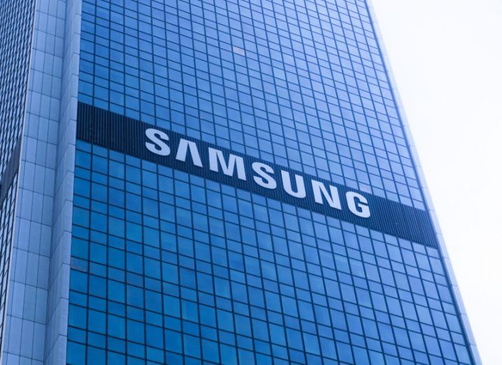 The Samsung logo on the side of a tall windowed building, with a bright grey sky in the background.