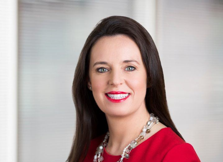 Headshot of Anna Scally of KPMG Ireland, wearing a red shirt with a grey wall in the background.